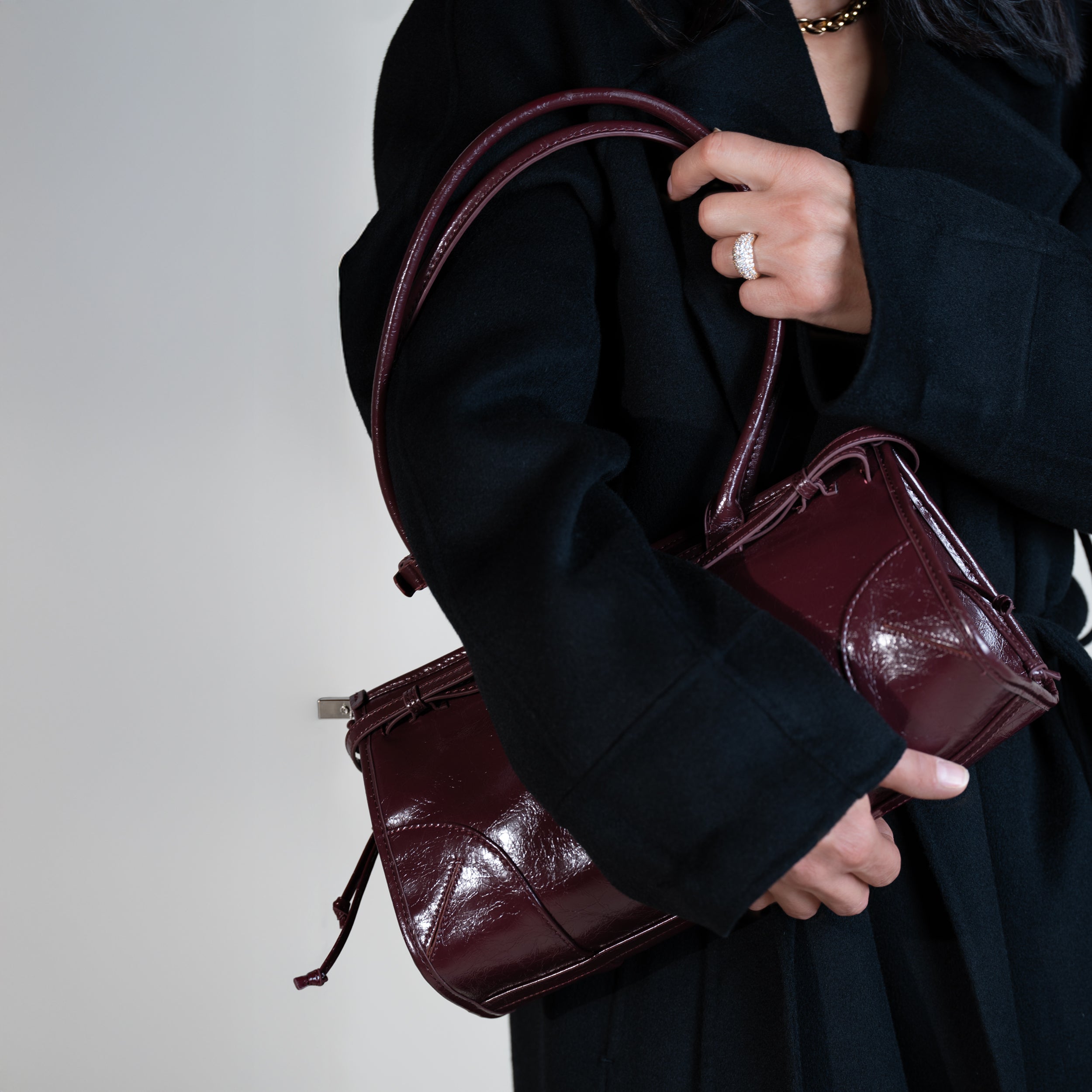 sac à main forme baguette femme en cuir verni bordeaux vintage porté à l'épaule sur un manteau noir avec une bague en diamant