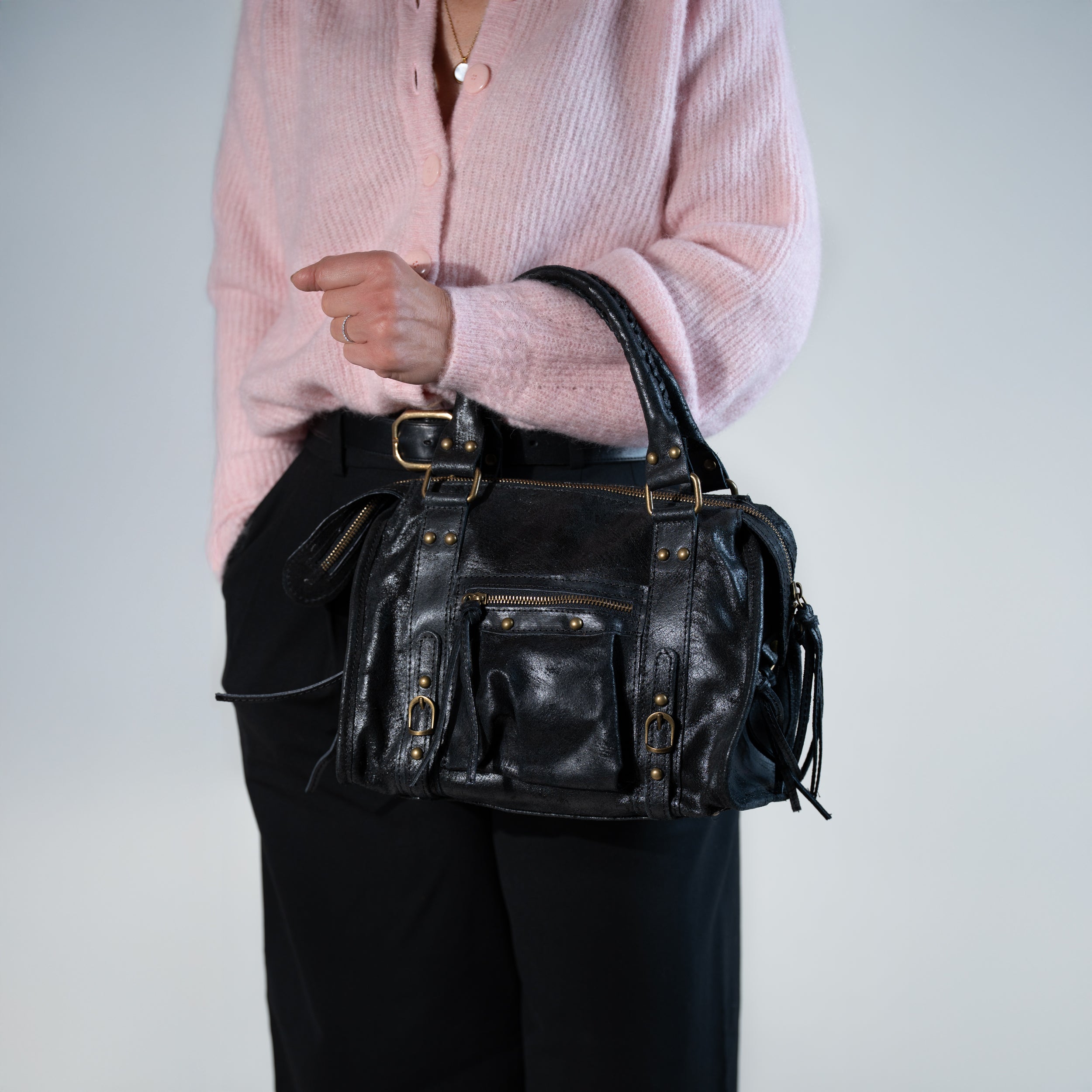 sac à main femme forme bowling vintage en cuir vieilli noir dans un cuir de veau souple porté au creux de bras avec un pull en laine rose et un pantalon noir