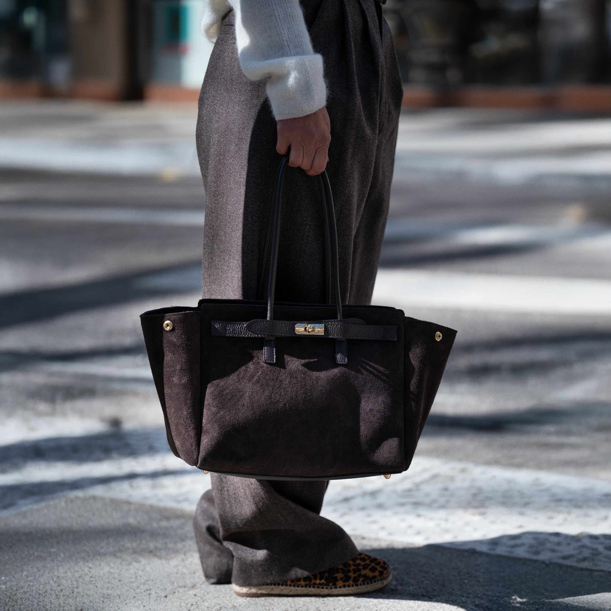 sac cabas femme en cuir suédé ou daim brun en forme rectangulaire avec fermoir tourniquet porté à la main sur un pantalon tailleur marron avec chaussure léopard