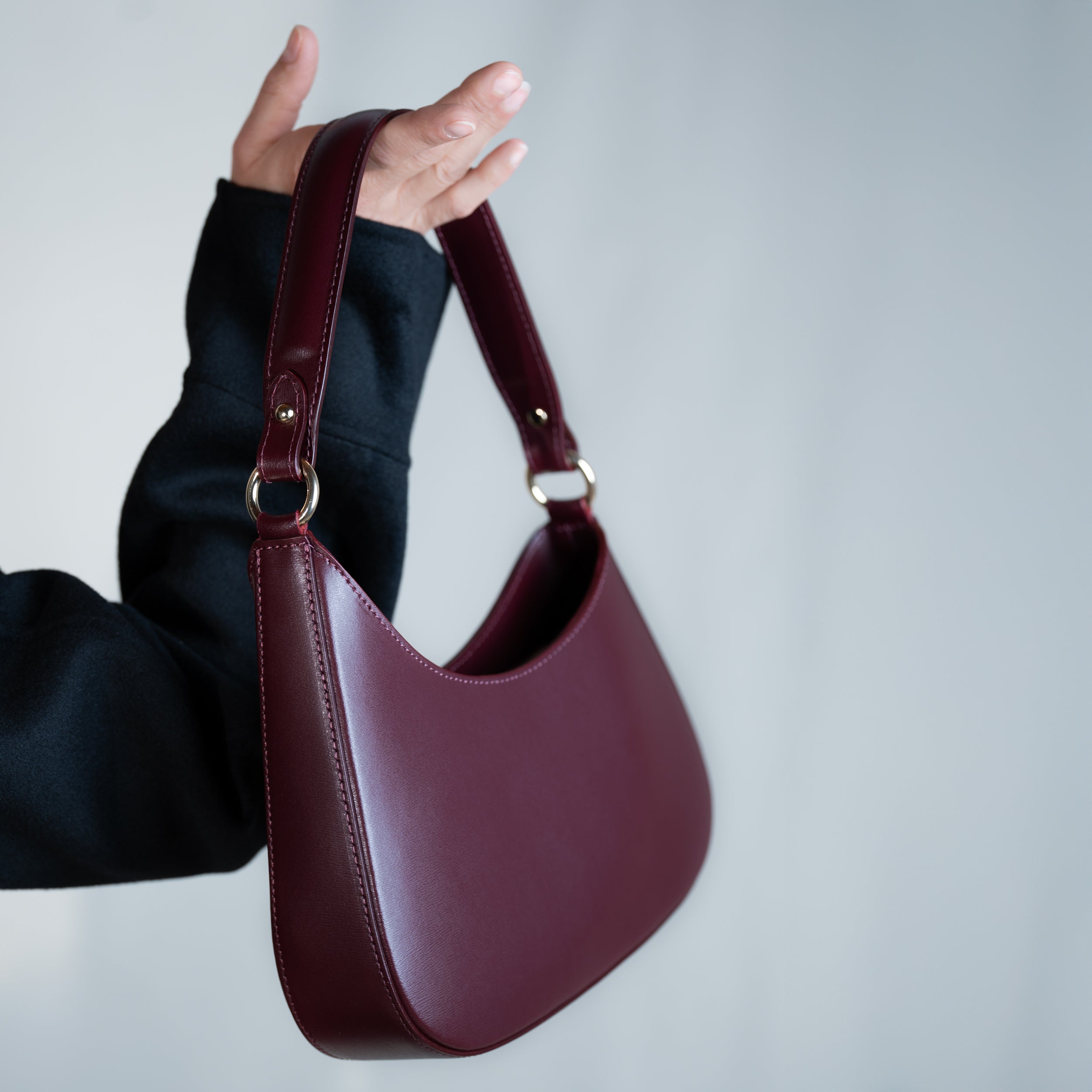 sac à main forme hobo demi lune asymétrique pour femme en cuir lisse bordeaux porté à la main