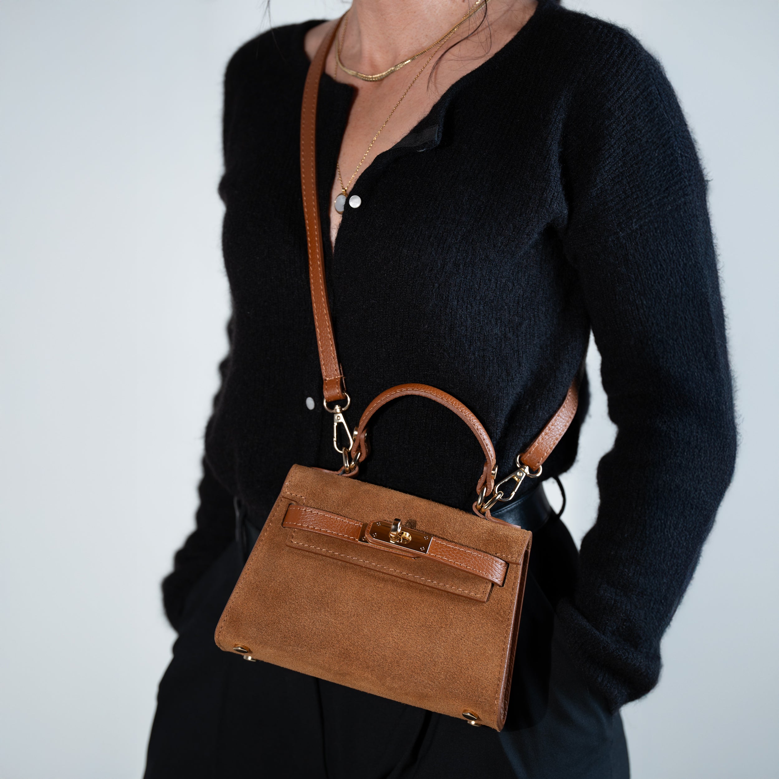sac à main femme en daim top handle avec fermoir tourniquet et bijouterie doré dans un cuir suédé camel porté en bandoulière sur un pull noir et un pantalon noir
