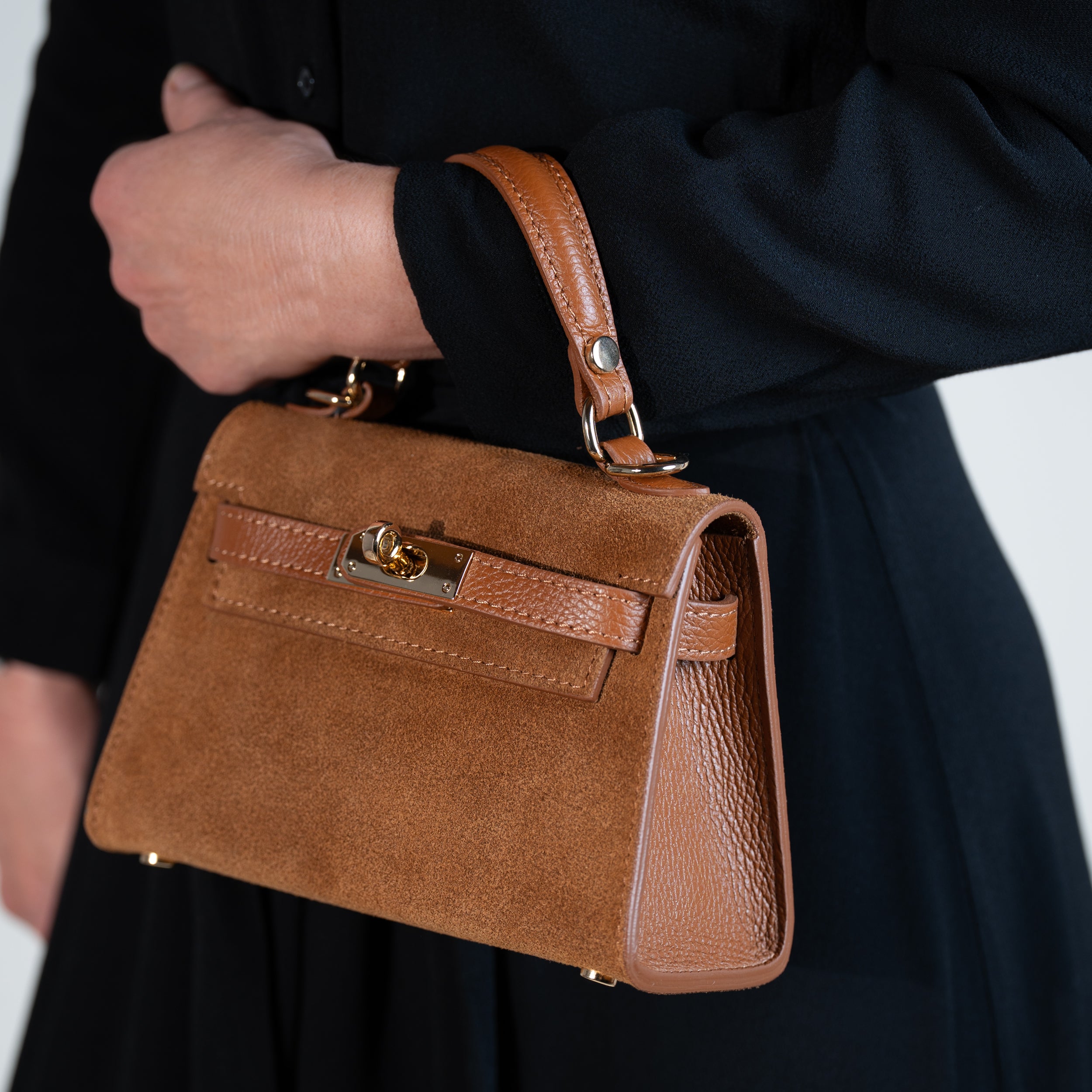 sac à main femme en daim top handle avec fermoir tourniquet et bijouterie doré dans un cuir suédé camel porté au poignet  sur une robe noir