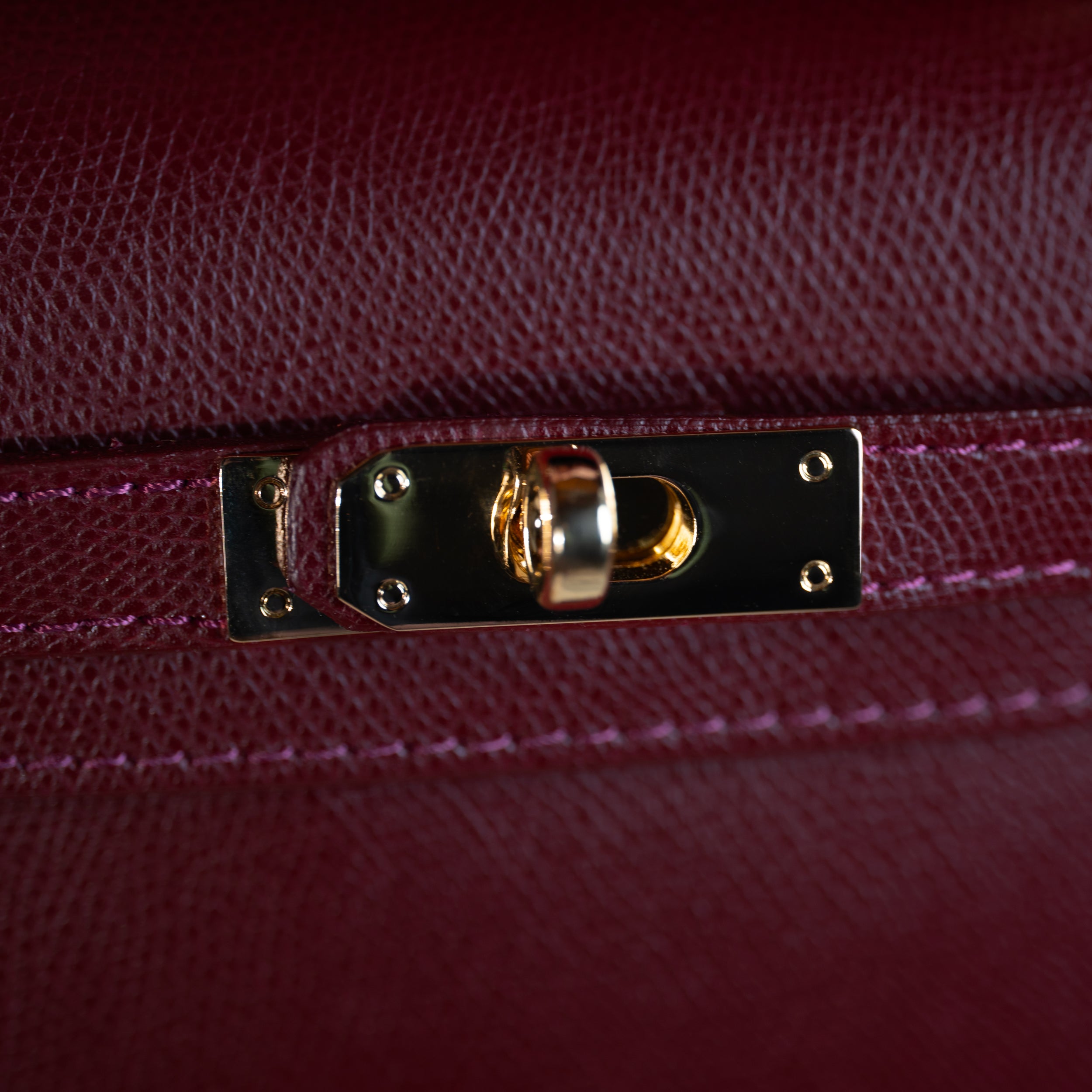 zoom sur le cuir saffiano d'un sac à main top handle avec focus sur son fermoir tourniquet doré et son cuir de qualité bordeaux 