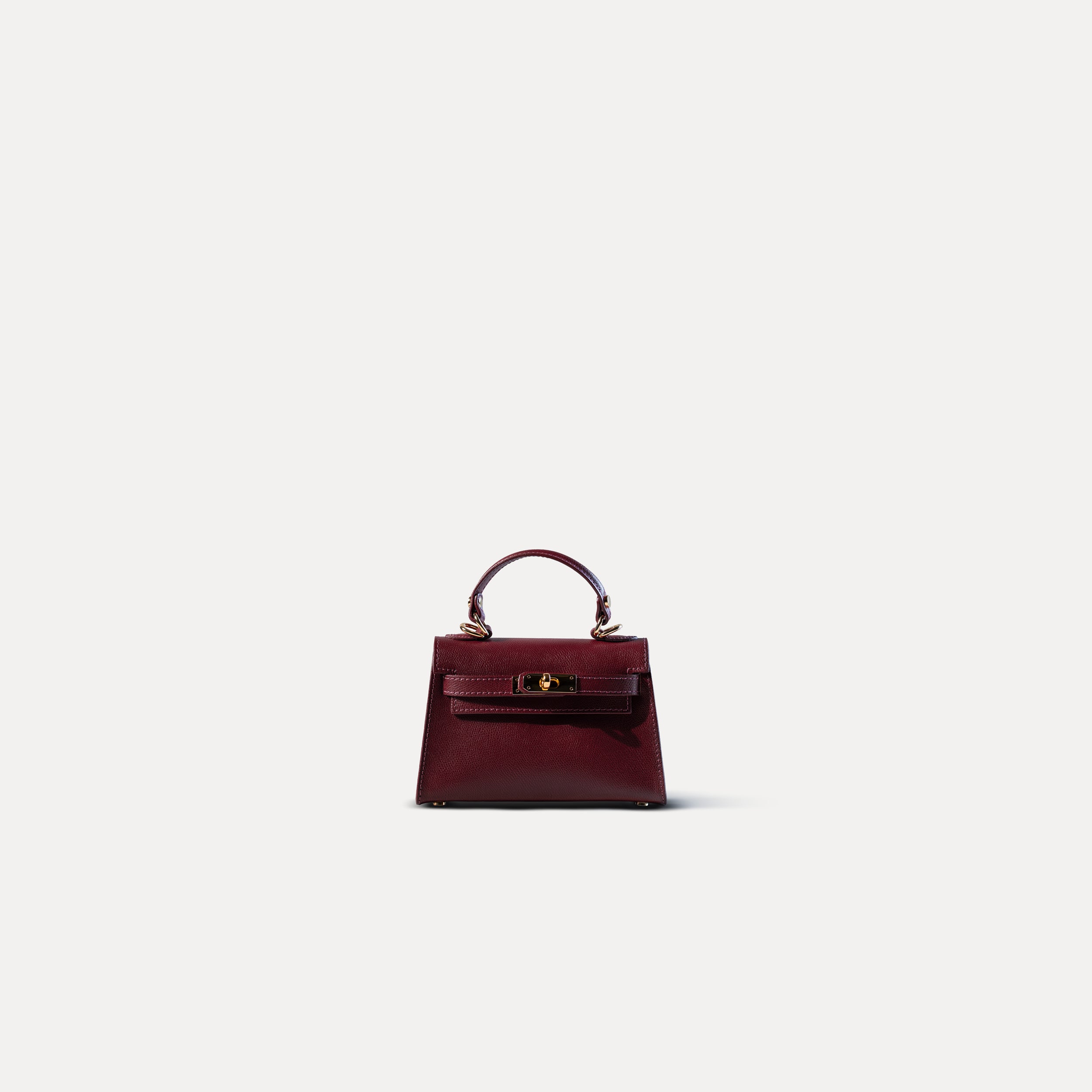 sac à main femme en cuir saffiano bordeaux top handle avec fermoir tourniquet et bijouterie doré sur fond blanc